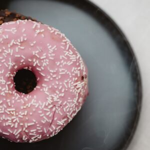 Top view of a pink sprinkled donut with a chocolate one beneath on a plate.